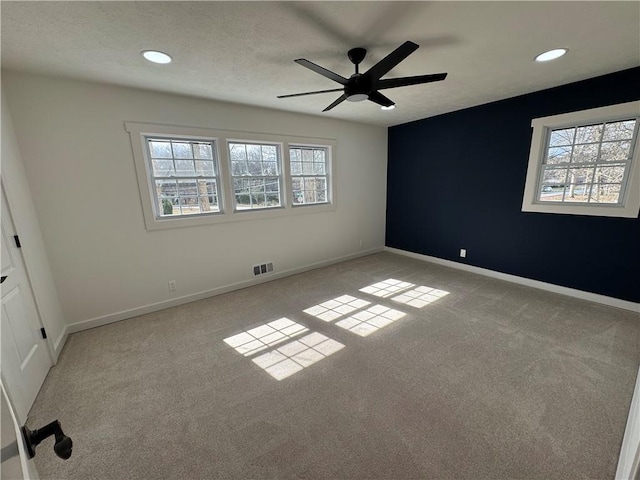 spare room with baseboards, light colored carpet, visible vents, and a healthy amount of sunlight