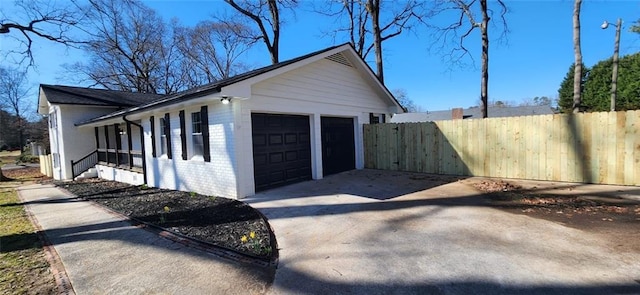 exterior space featuring concrete driveway, brick siding, an attached garage, and fence