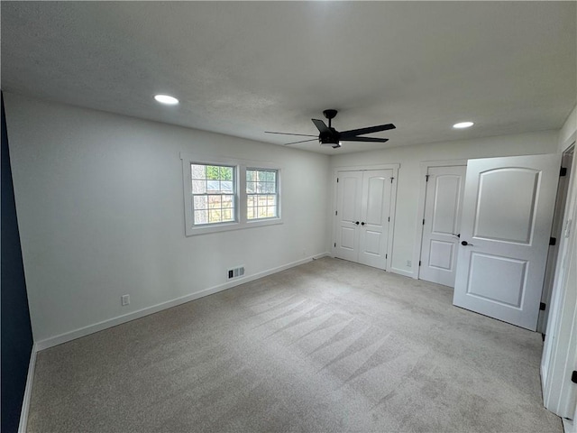 unfurnished bedroom with two closets, recessed lighting, light colored carpet, visible vents, and baseboards