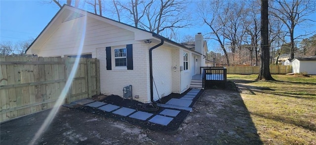 view of side of home with a yard, brick siding, a chimney, and fence