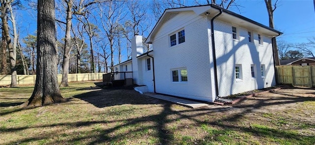 back of house with brick siding, a chimney, a fenced backyard, and a lawn