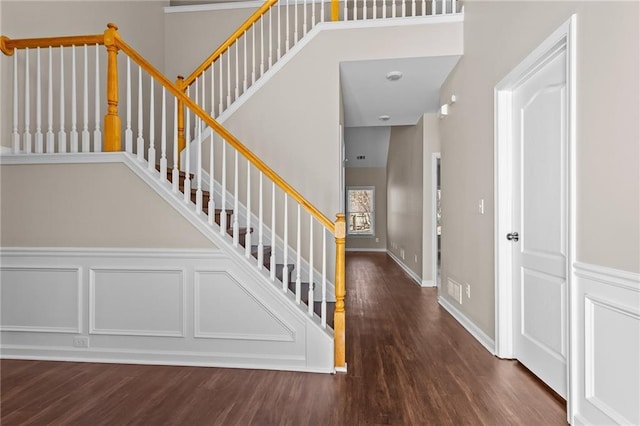 staircase featuring a decorative wall, a towering ceiling, baseboards, and wood finished floors