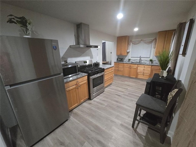 kitchen with light wood-style flooring, stainless steel appliances, a sink, wall chimney exhaust hood, and brown cabinetry