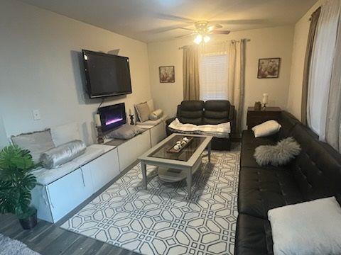 living room with a ceiling fan, a lit fireplace, and wood finished floors