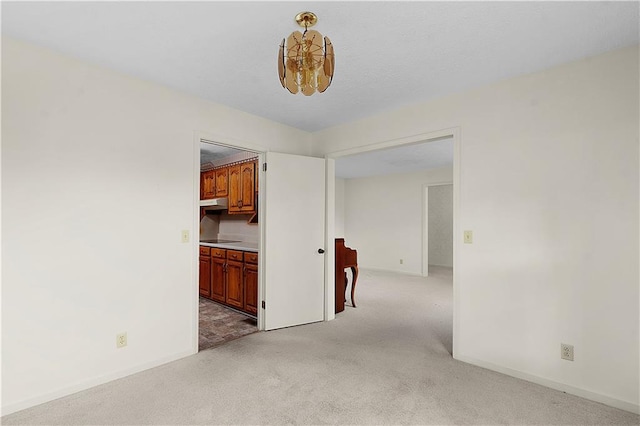 spare room featuring light carpet and a notable chandelier