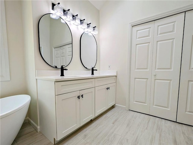 bathroom featuring baseboards, double vanity, a sink, and a freestanding bath