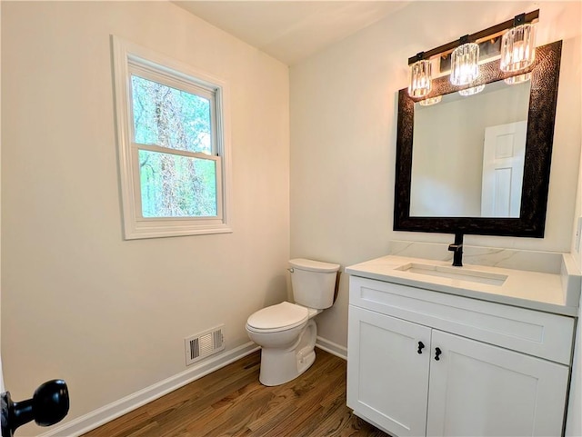 bathroom with toilet, vanity, wood finished floors, baseboards, and visible vents