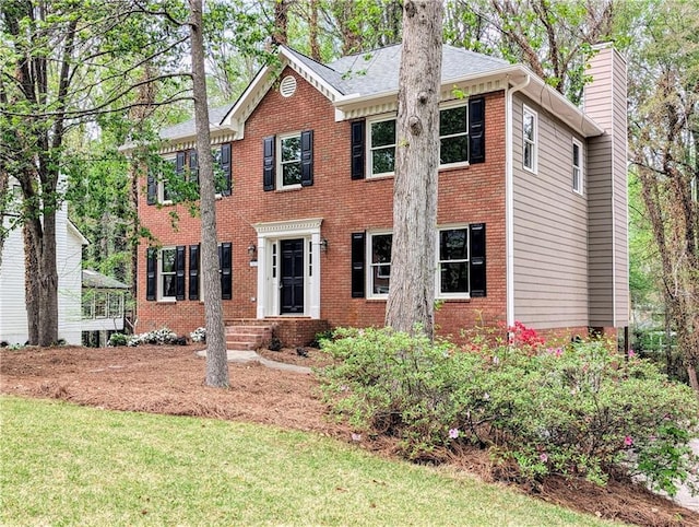 colonial-style house with brick siding, a chimney, and a front yard