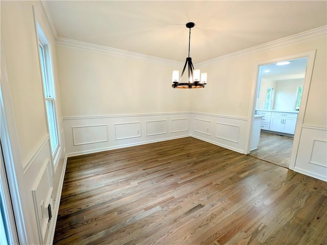 unfurnished dining area featuring a decorative wall, wood finished floors, an inviting chandelier, and crown molding