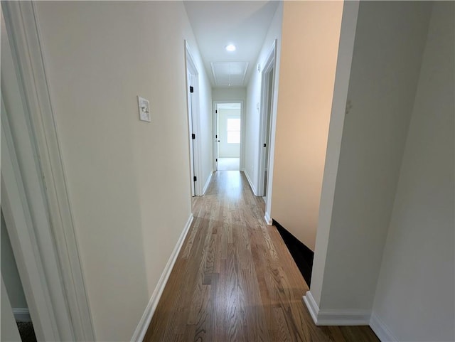 hall featuring light wood-style floors, baseboards, and attic access