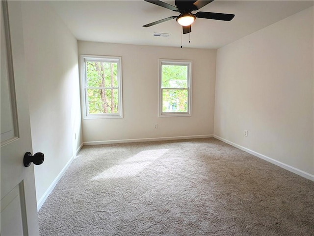empty room with carpet flooring, visible vents, a healthy amount of sunlight, and a ceiling fan