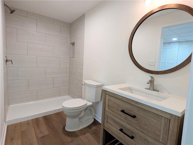 bathroom with toilet, vanity, tiled shower, and wood finished floors