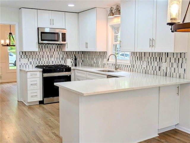 kitchen with a sink, white cabinetry, light wood-type flooring, gas range oven, and stainless steel microwave
