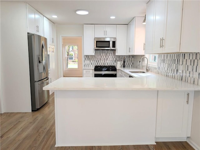 kitchen with backsplash, a sink, light wood finished floors, a peninsula, and stainless steel appliances