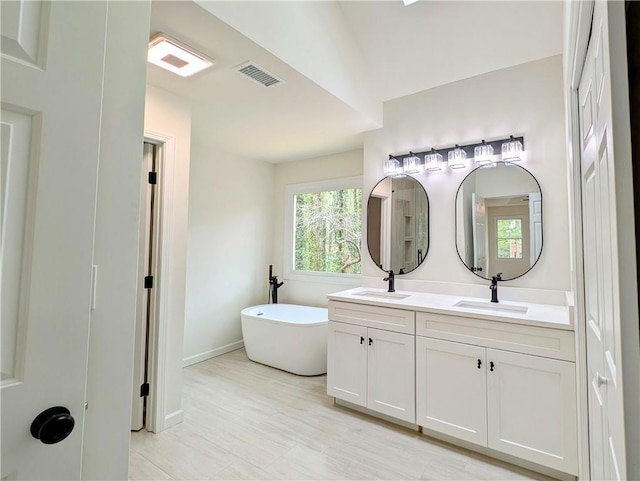 bathroom with a soaking tub, double vanity, visible vents, and a sink