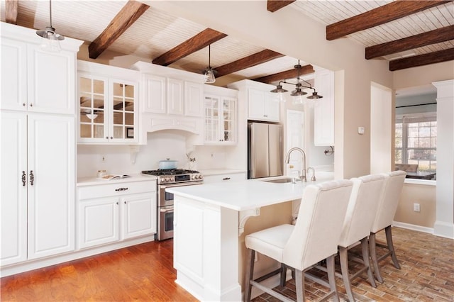 kitchen with sink, decorative light fixtures, appliances with stainless steel finishes, a kitchen island with sink, and white cabinets