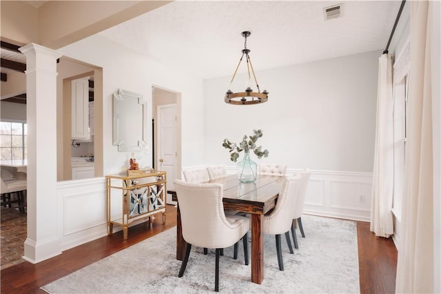 dining room with decorative columns, dark wood-type flooring, and a notable chandelier