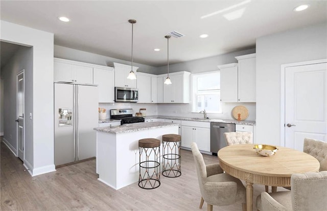 kitchen with sink, a kitchen island, pendant lighting, appliances with stainless steel finishes, and white cabinetry