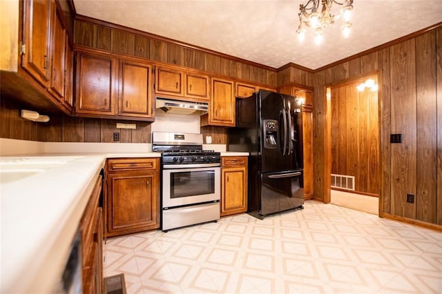 kitchen featuring wooden walls, stainless steel gas stove, ornamental molding, black fridge with ice dispenser, and a textured ceiling