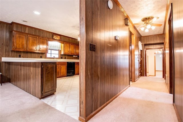 kitchen with wooden walls, kitchen peninsula, crown molding, light carpet, and a textured ceiling