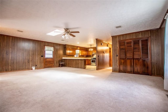 unfurnished living room with ceiling fan, a skylight, wooden walls, a textured ceiling, and light carpet