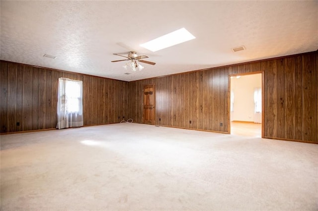 carpeted empty room with ceiling fan, a skylight, and a textured ceiling