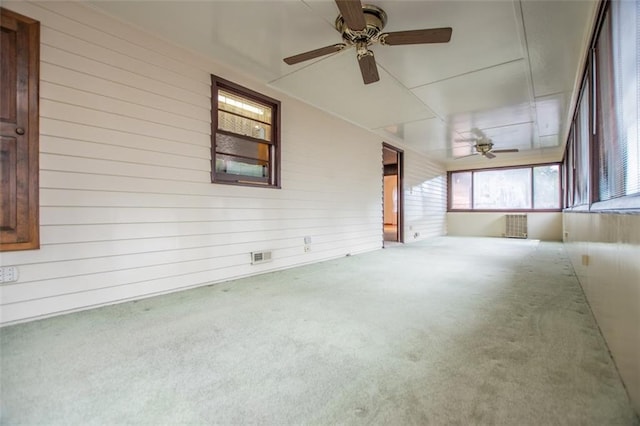 empty room featuring ceiling fan, wooden walls, carpet flooring, and radiator