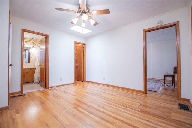 unfurnished bedroom featuring ceiling fan, ensuite bath, a skylight, and light hardwood / wood-style floors