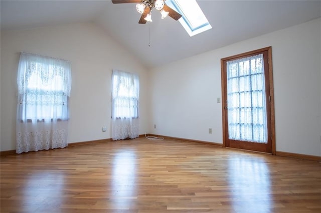 empty room with ceiling fan, plenty of natural light, vaulted ceiling with skylight, and light hardwood / wood-style floors