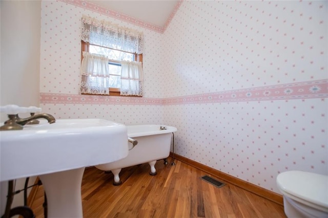 bathroom with wood-type flooring, a tub, and toilet