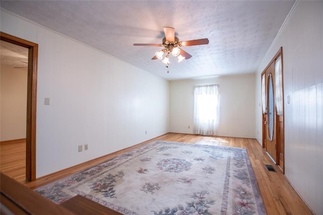 empty room with ceiling fan, wooden walls, ornamental molding, light hardwood / wood-style floors, and a textured ceiling