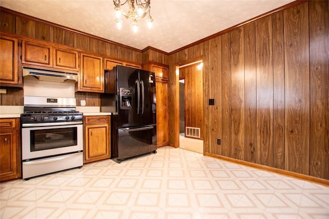 kitchen featuring stainless steel gas stove, black fridge, crown molding, a chandelier, and wooden walls