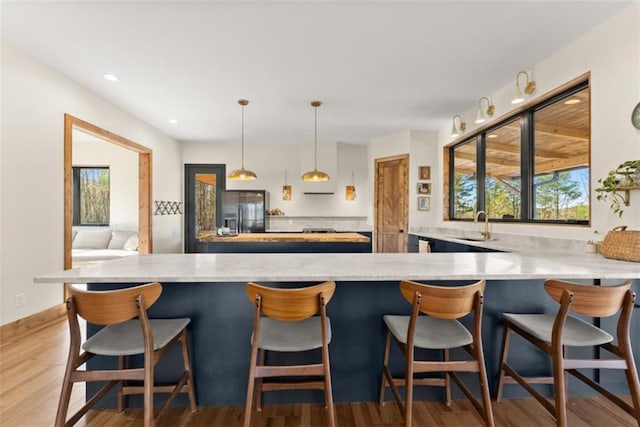 kitchen featuring a kitchen breakfast bar, stainless steel fridge, kitchen peninsula, and hanging light fixtures