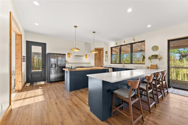 kitchen featuring a breakfast bar, stainless steel fridge, hanging light fixtures, kitchen peninsula, and light wood-type flooring