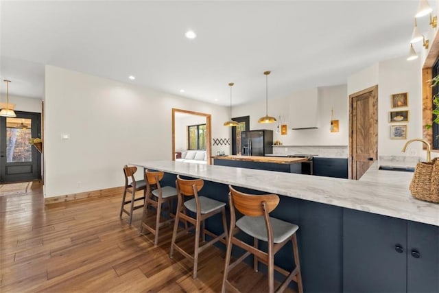 kitchen with sink, black fridge, light stone counters, decorative light fixtures, and hardwood / wood-style floors