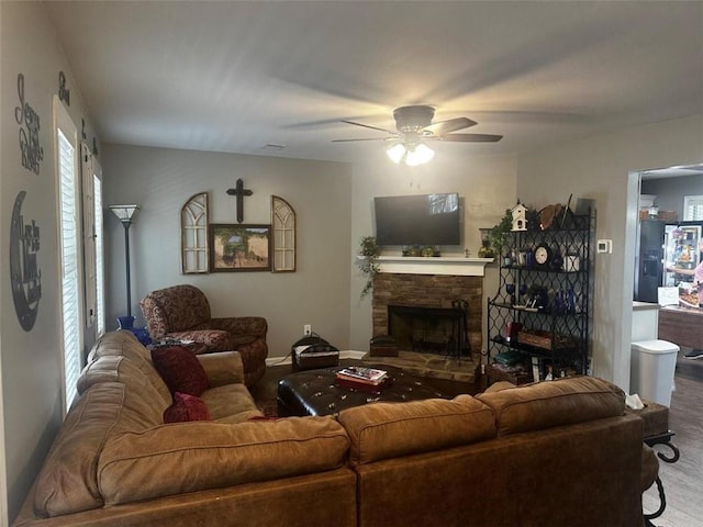 living room featuring hardwood / wood-style flooring, ceiling fan, and a stone fireplace