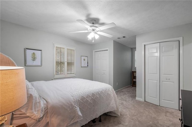 carpeted bedroom with a textured ceiling, ceiling fan, and two closets