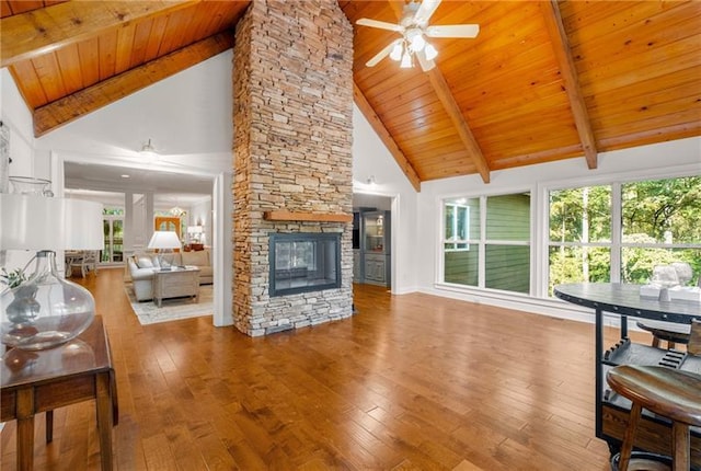 living room featuring beam ceiling, high vaulted ceiling, wooden ceiling, and a stone fireplace