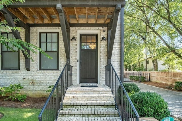 view of exterior entry with stone siding and fence