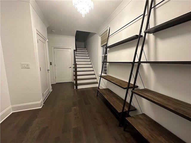 corridor featuring wood finished floors, baseboards, stairs, ornamental molding, and an inviting chandelier