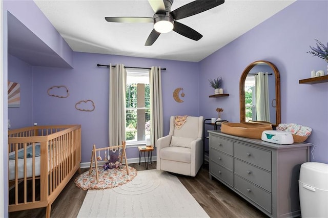 bedroom with dark hardwood / wood-style flooring, a nursery area, and ceiling fan