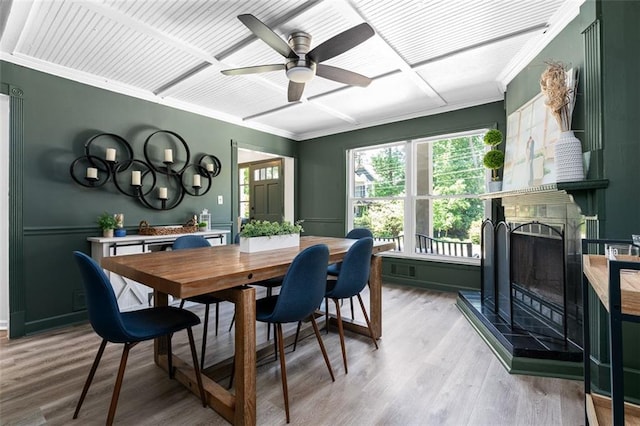 dining area with ceiling fan, light hardwood / wood-style floors, ornamental molding, and a tiled fireplace