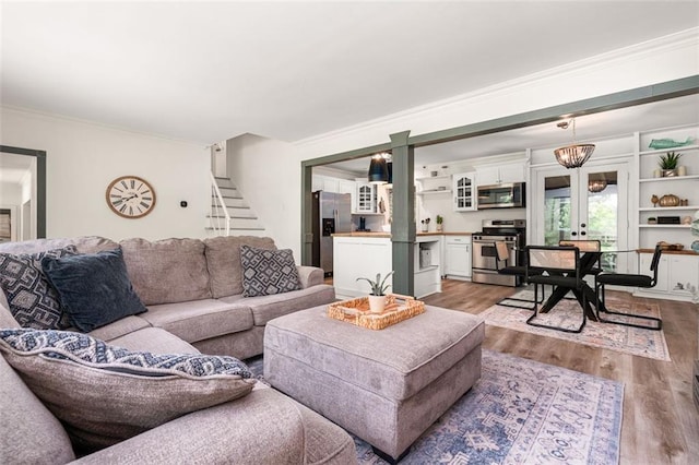 living room featuring french doors, light wood-type flooring, crown molding, and an inviting chandelier