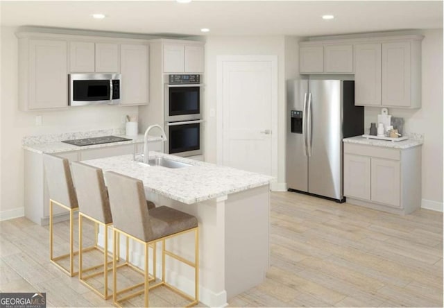 kitchen featuring light stone counters, a center island with sink, light wood finished floors, stainless steel appliances, and recessed lighting