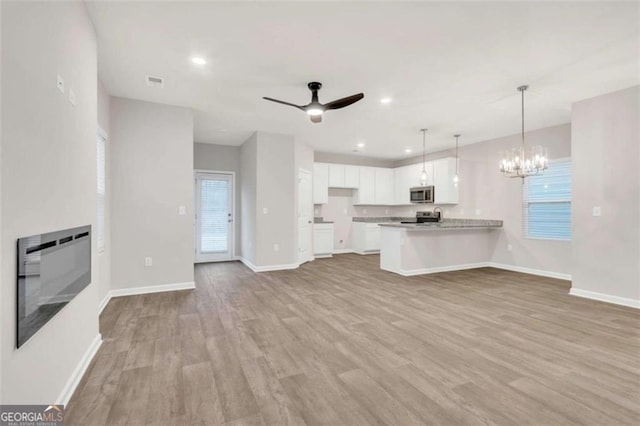 kitchen with a peninsula, white cabinets, open floor plan, appliances with stainless steel finishes, and a glass covered fireplace