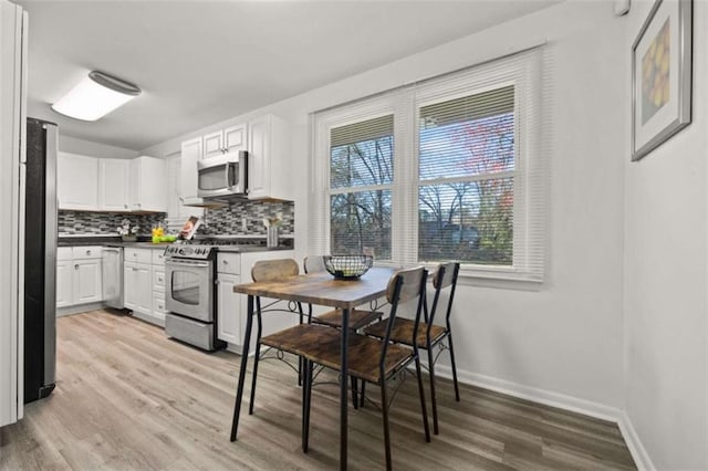 kitchen with baseboards, stainless steel appliances, decorative backsplash, light wood-style floors, and dark countertops