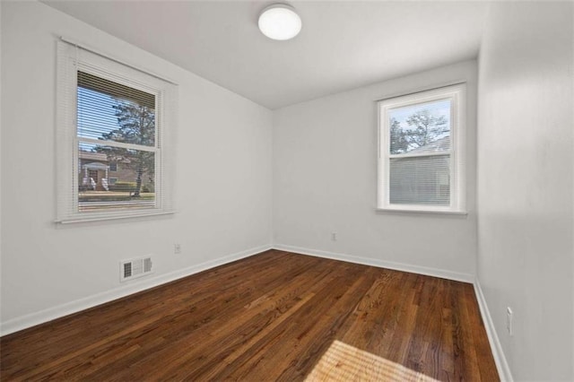 spare room featuring wood finished floors, a healthy amount of sunlight, visible vents, and baseboards