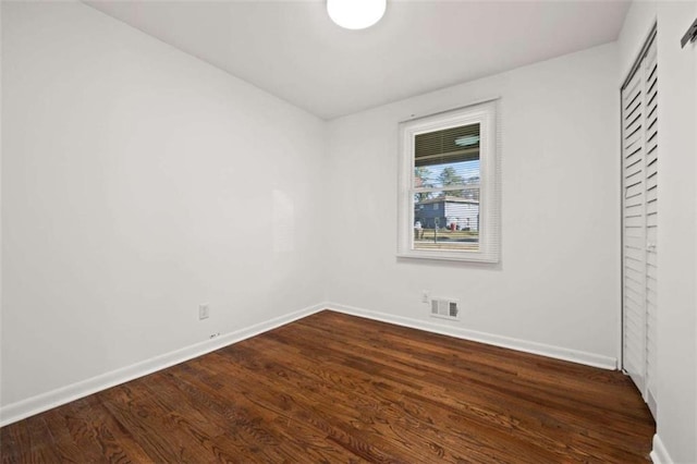 unfurnished room featuring dark wood-style floors, visible vents, and baseboards