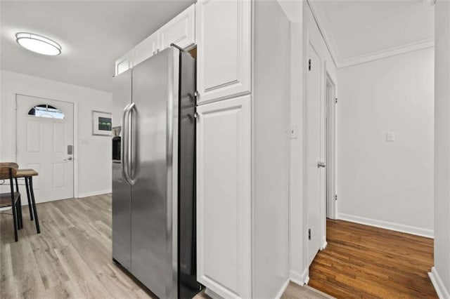 kitchen featuring stainless steel fridge, white cabinets, light wood-type flooring, and baseboards