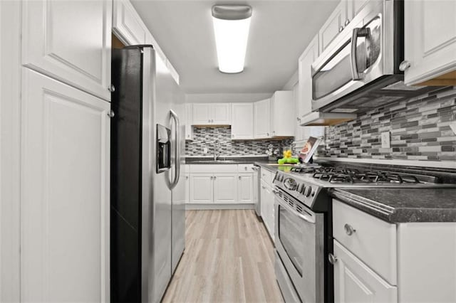 kitchen with dark countertops, backsplash, light wood-type flooring, appliances with stainless steel finishes, and white cabinets